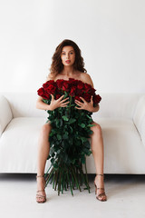 Brunette on a white sofa with a large bouquet of red roses