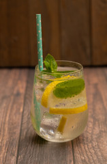 A glass of cold water with ice cubes, lemon, and mint