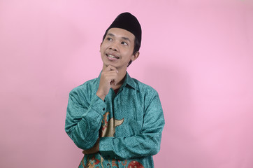 The young man seemed to think and look up. Portrait of young Asian man wearing batik shirt and skullcaps isolated on a pink background