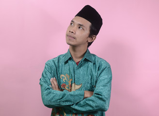 The young man seemed to think and look up. Portrait of young Asian man wearing batik shirt and skullcaps isolated on a pink background