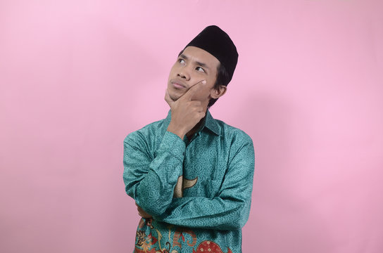 The young man seemed to think and look up. Portrait of young Asian man wearing batik shirt and skullcaps isolated on a pink background