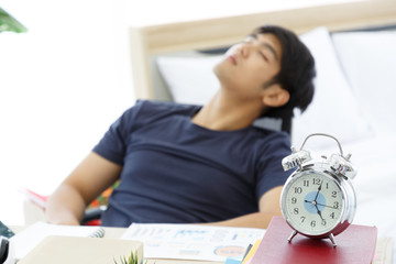 Clock on Table in front of Tired Asian man napping at a office after a hard workday, working on desk, tried, Work From Home.
