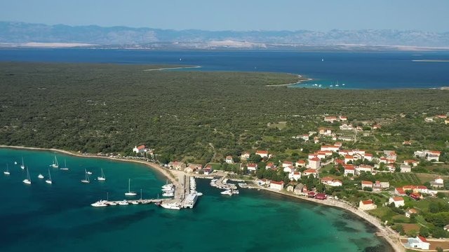 The Lush Island Of Olib In Croatia - Sailboats, And Tourist Boats On The Shallow Blue Sea Water At The Pier - aerial shot