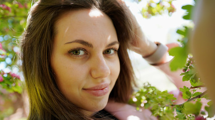 Portrait of pretty girl among branches of blossoming tree in spring in park