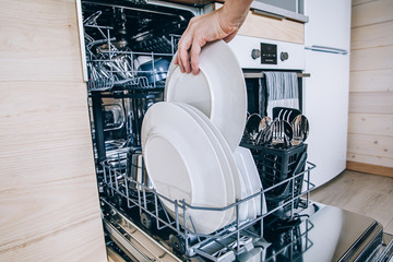 Woman loading the dishwasher. Open dishwasher with clean glasses and dishes close-up after washing.