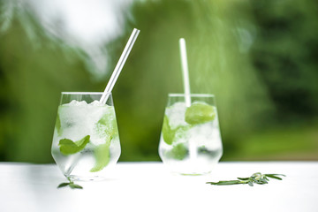 Beautiful glass of water or mojito with lime and mint cocktail on the gree background and white table summer vibe and atmosphere
