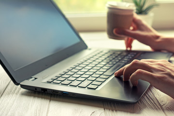 Young adult sitting in freelance home office with black laptop and cup of coffee or tea