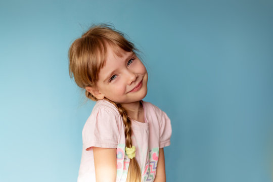 Little girl shaggy with pigtails smiling, looking at the camera, close-up, blue background