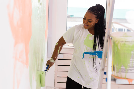 Happy smiling african american woman painting interior wall of new house. Redecoration, renovation, apartment repair and refreshment concept.