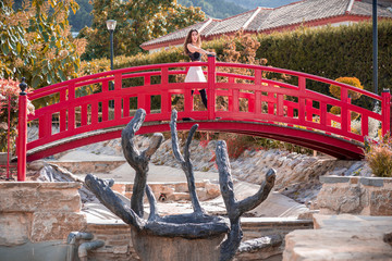 Pretty woman with miniskirt posing on a red bridge in a Japanese garden