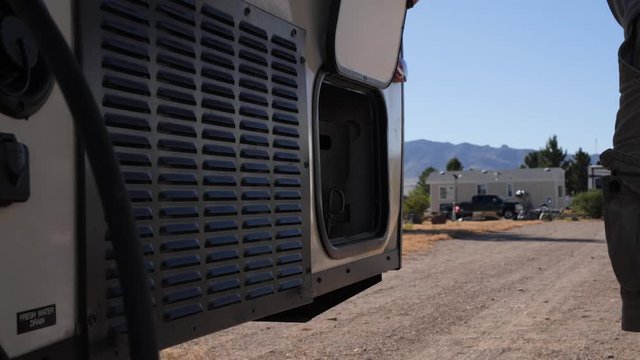 A man getting a tool out of a compartment while camping in a RV trailer