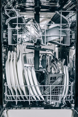 Open dishwasher with clean glasses and dishes close-up after washing.