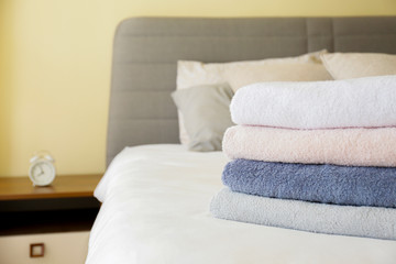 Hotel room with freshly made bed, perfectly clean and ironed sheets, stack of new folded towels in natural sun light. Close up, copy space for text.