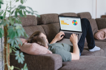 mann liegt auf der Couch und arbeitet im Homeoffice am laptop