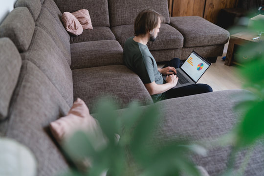 mann sitzt an der Couch und arbeitet im homeffice am laptop, blick von hinten