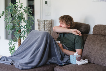 mann sitzt mit einer Grippe auf der Couch und hustet in die  Armbeuge