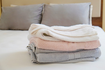 Hotel room with freshly made bed, perfectly clean and ironed sheets, stack of new folded towels in natural sun light. Close up, copy space for text.