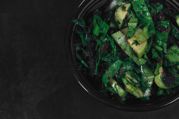 Bowl with salad of organic vegetables and herbs on dark textured background. Top View, space for text. Organic eco food. Carrots with green tops tied with rope. Healthy diet. Freshly cut vegetables