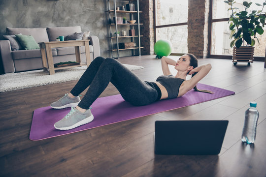 Full size photo of focused active sporty athletic beautiful girl doing video online workout laptop aerobics exercise crunches pilates on floor mat in house indoors
