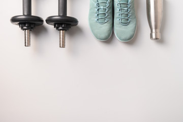 Sport and fitness equipment, dumbbells, shoes, water bottle on grey. Top view, space for your text.