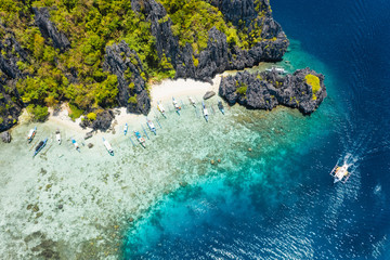 Aerial drone view tourism boats moored at tropical Shimizu Island. Limestone coastal rocks, white sand beach in blue water. El Nido, Palawan, Philippines
