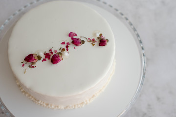 Fototapeta na wymiar White mousse cake decorated with dried rose buds with milk and berry filling, close up. Copy space, place for text