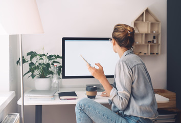Woman using smartphone while working on computer in home office.