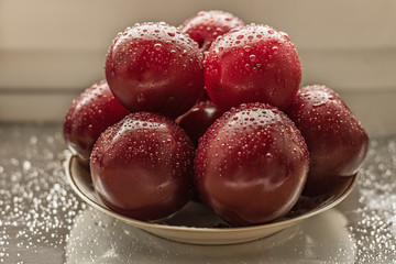 Satsuma red plum on a plate with water droplets.