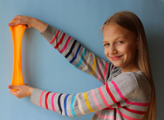 A blonde preteen girl playing with handmade orange slime on blue background. Activities and...
