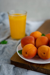 Ripe whole apricots on white plate on wooden cutting board against a glass of orange juice