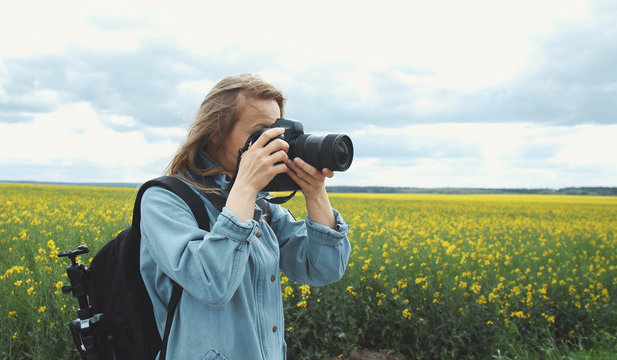 Female photographer taking pictures using dslr camera standing on rapeseed blooming field background