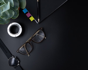 Flat lay, Office leather business table black desk, Bright Creative workspace with eyeglasses, black pen, notebook, camera lens, smartwatch and green plant with the sunlight, Top view with copy space