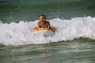 Cheerful kid riding on the foam wave on the bodyboard