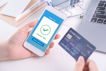 Electronic payment concept, online paying with smart phone, shopping with credit card, laptop over white table background with shop cart trolley, close up.
