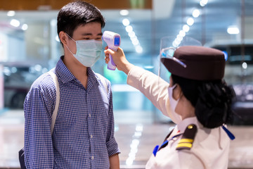 Security guard using infrared thermometer to measure body temperature check asian people in medical protective mask before access to office building for against epidemic flu Coronavirus (CoVID-19) 
