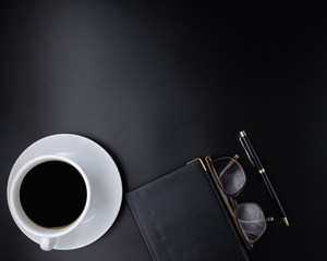 Flat lay, Office leather business table black desk, Bright Creative workspace with eyeglasses, a cup of black coffee, notebook, the pen with the sunlight, Top view with copy space