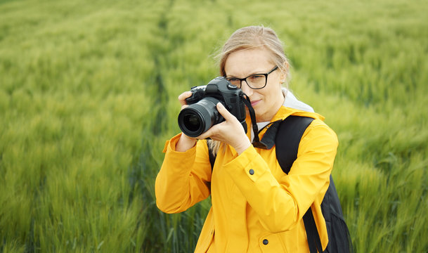 Female photographer standing in greenery taking pictures using dslr, selective focus