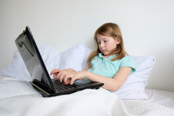 little girl sitting at a laptop and doing homework. baby with laptop in bed