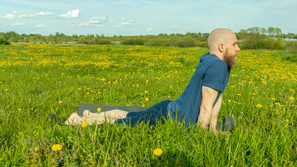 A bald man with a beard does yoga in nature