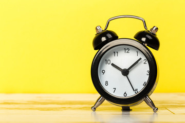 Black retro alarm clock with bells on a wooden table, daily routine concept.