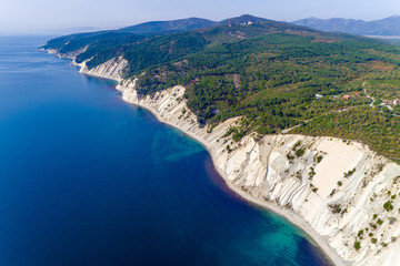 Obraz premium The coast of the Black sea near Gelendzhik. High layered rocks covered with pine trees. Gorges form a descent to the sea. A small pebble beach at the foot of the cliffs