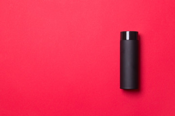 black thermos cup on red colored paper background background with copy space