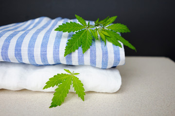 
white and striped fabric with fresh hemp leaves. The concept of using hemp for making fabrics and clothes