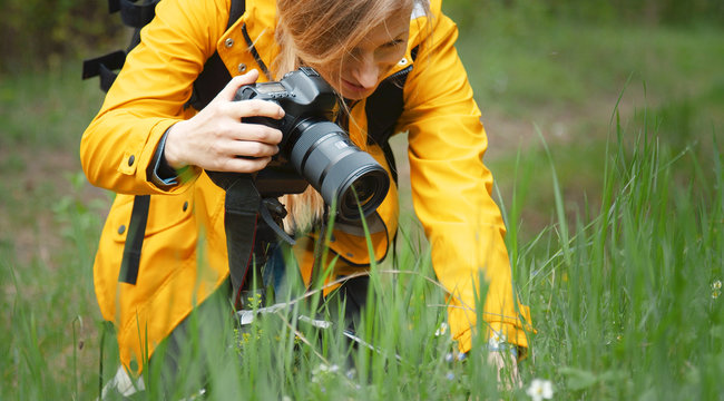 Close-up of female photographer making macrography using dslr camera kneeling in spring nature