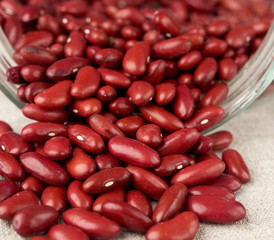 scattered red raw beans from a glass jar on a gray linen napkin