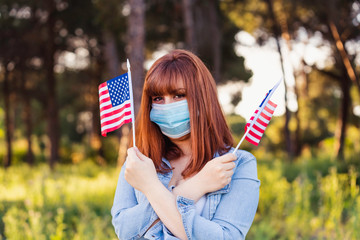 girl in protective medical mask with flags of United States of America in hands in nature. July 4 United States Independence Day. Health protection, safety and pandemic concept