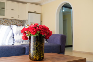 Empty apartment with minimalistic style interior, coffee table with bouquet in glass vase on foreground. Copy space for text, background, close up.