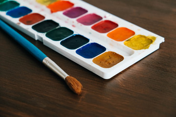 Set of watercolor paints with a brush for painting on a dark wooden background. Copy, empty space for text