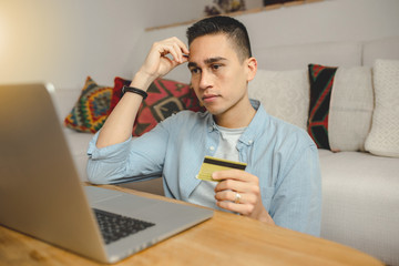 Young man using laptop computer at home. Holding credit card. Freelance, student lifestyle, education, technology and online shopping concept.