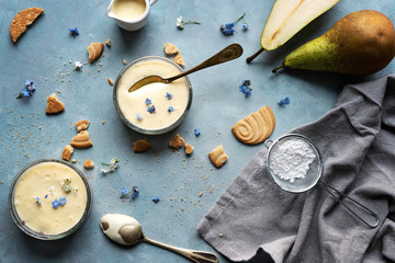 Healthy homemade dessert in jars made from vanilla pudding, cookies and pear on blue background in rustic style. Sweet food for eating delicious meal. Top view. 